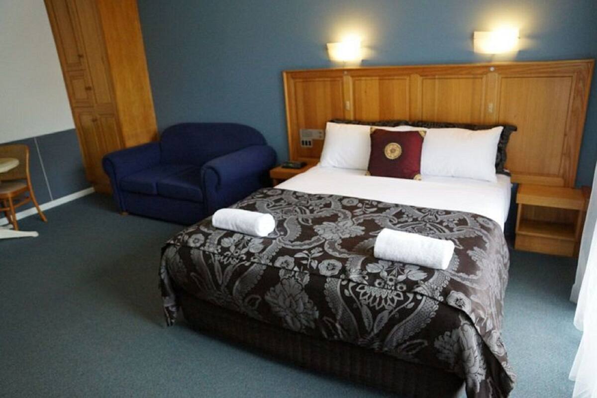 A hotel room with a large bed, a blue armchair, and a wooden headboard.