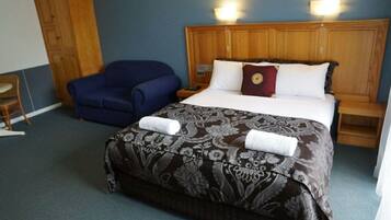 A hotel room with a large bed, a blue armchair, and a wooden headboard.