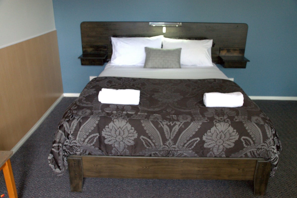 A neatly made bed with a patterned bedspread, two pillows, and two folded towels on the side.