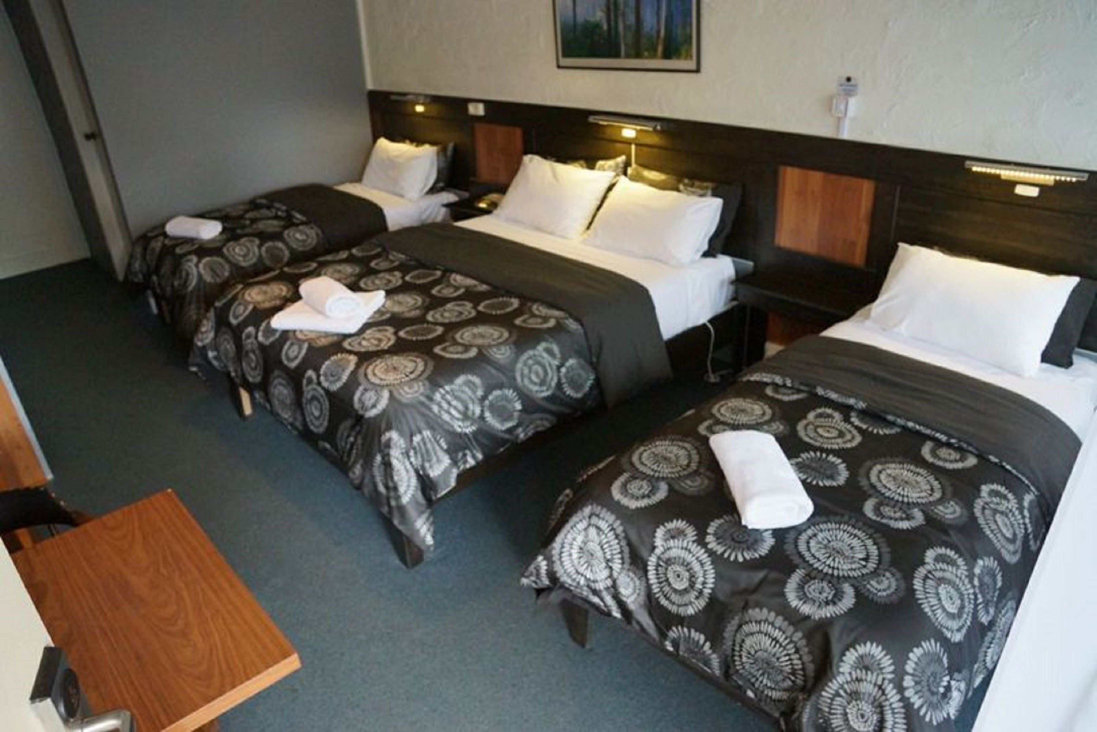 Une chambre d’hôtel avec deux lits simples, chacun agrémenté de draps à motifs et d’oreillers blancs. On y trouve une table d’appoint en bois et une table de chevet avec une lampe.
