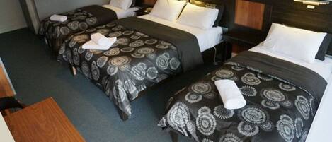 Une chambre d’hôtel avec deux lits simples, chacun agrémenté de draps à motifs et d’oreillers blancs. On y trouve une table d’appoint en bois et une table de chevet avec une lampe.