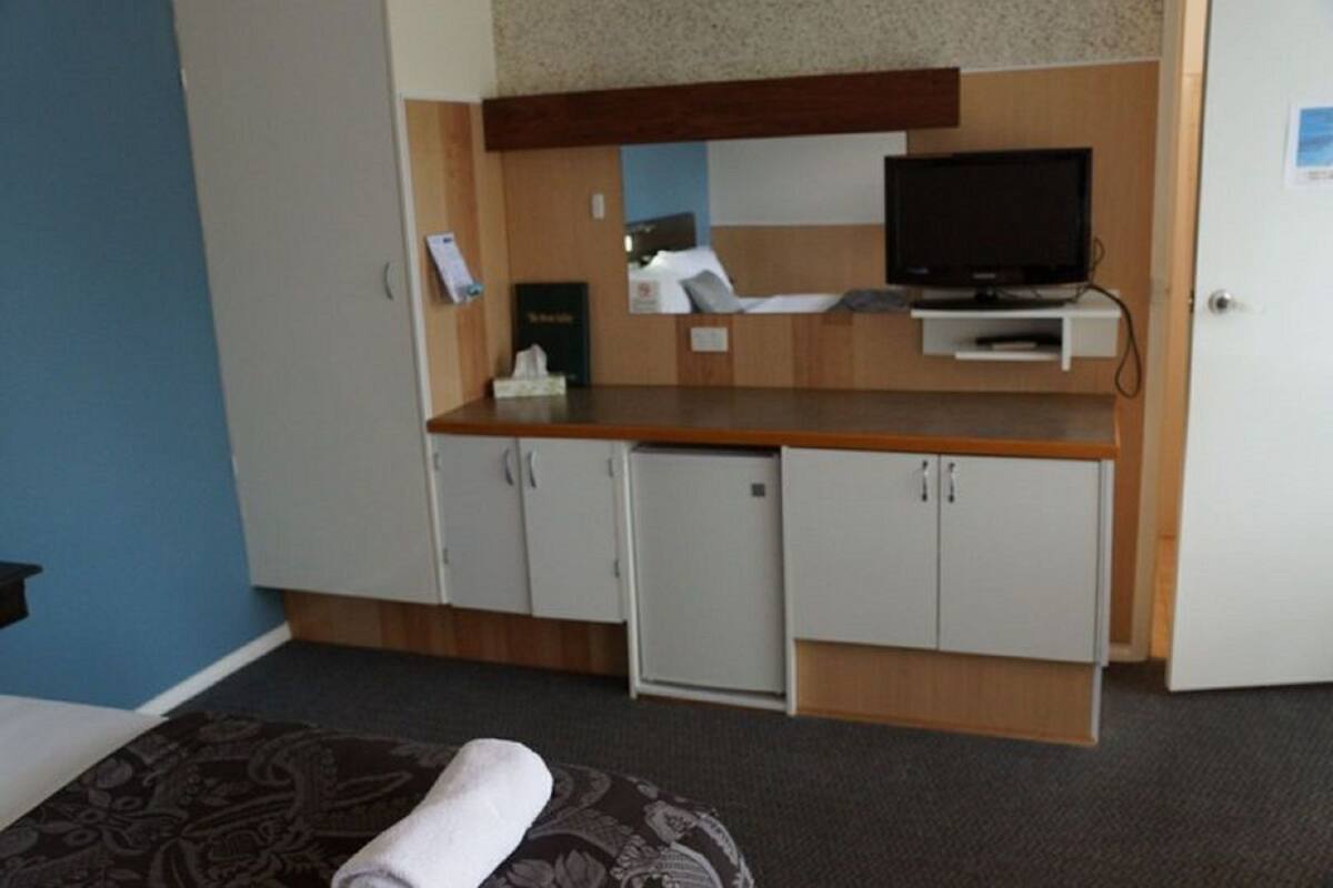 A hotel room with a bed, a small desk with a television, a minibar, and a door with a lock.