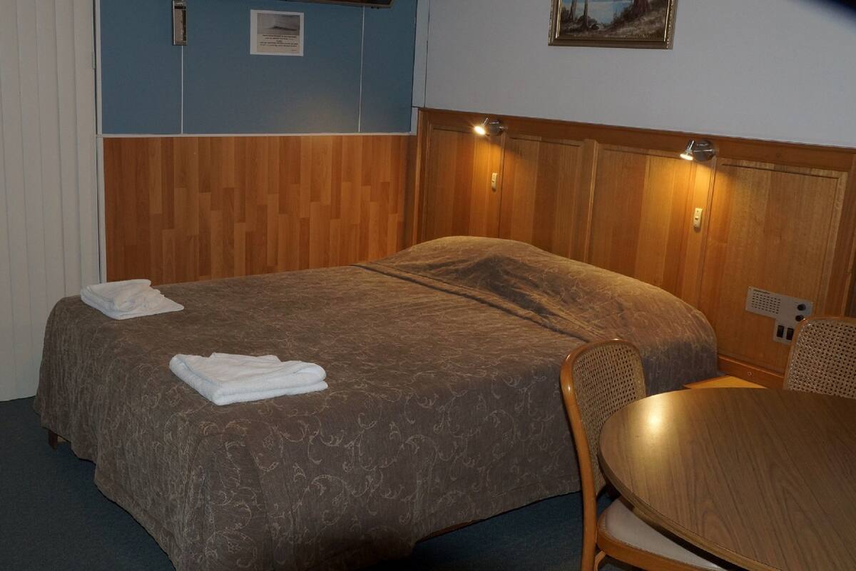 A hotel room with a bed, a chair, a table, and a painting on the wall.