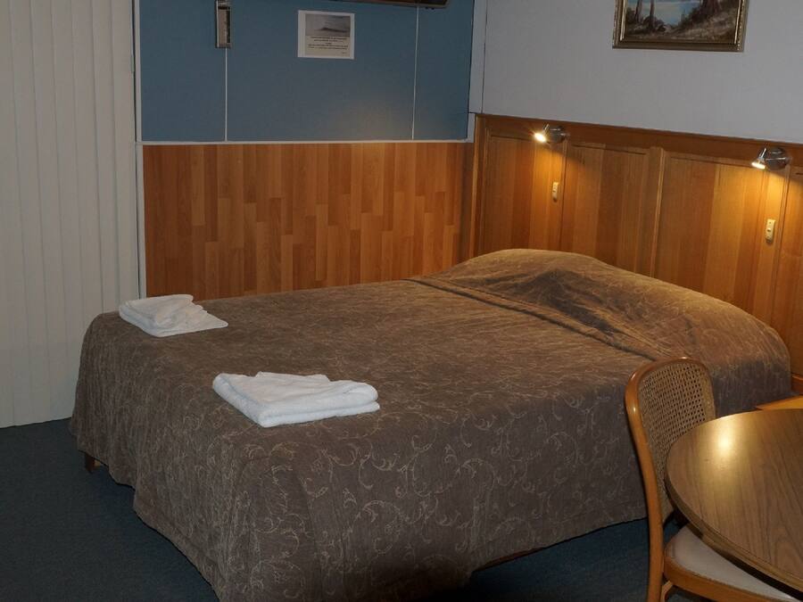 A hotel room with a bed, a chair, a table, and a painting on the wall.