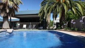 Una piscina con agua cristalina azul, rodeada de palmeras y un edificio de techo oscuro.