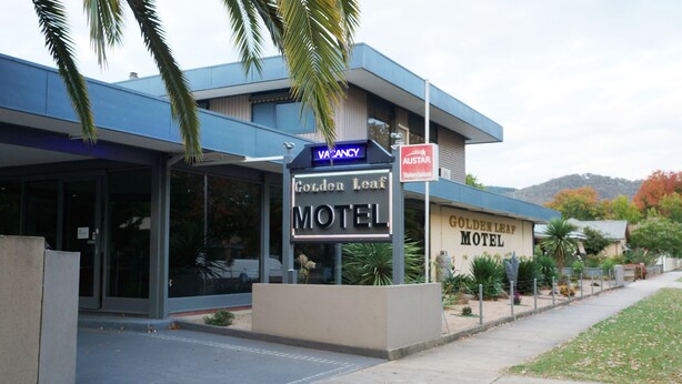 Un motel llamado 'Golden Leaf Motel' con un cartel de 'Habitación disponible' sobre la entrada.
