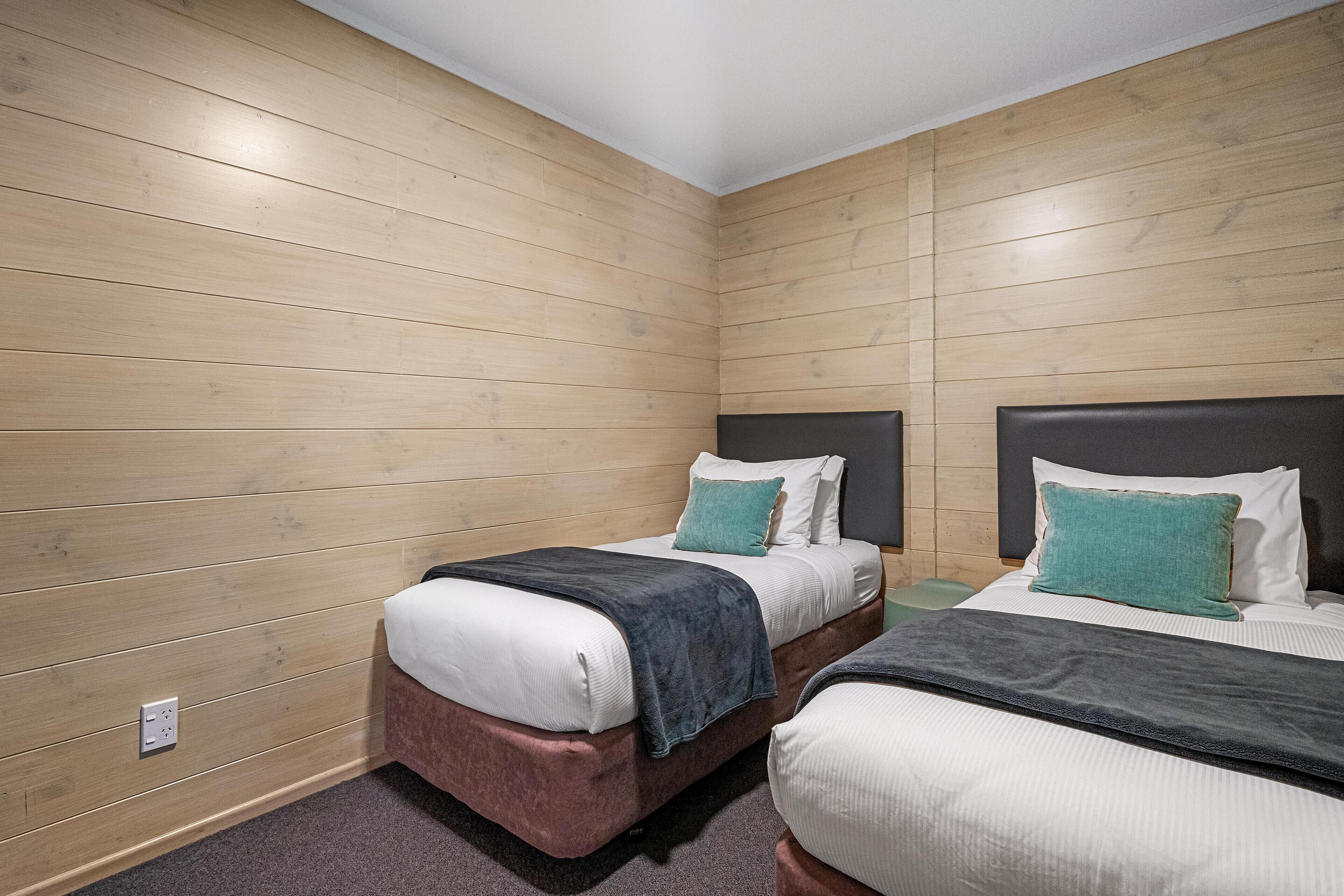 A room with two beds, wooden panel walls, and a power outlet on the left wall.