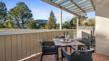 An outdoor patio with a covered table and chairs, a view of the street, and a wooden fence.