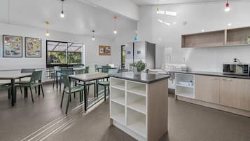 Een moderne keuken met witte kasten, een centraal eiland en een magnetron. Er staan groene stoelen rond een tafel en een raam met uitzicht op groen.