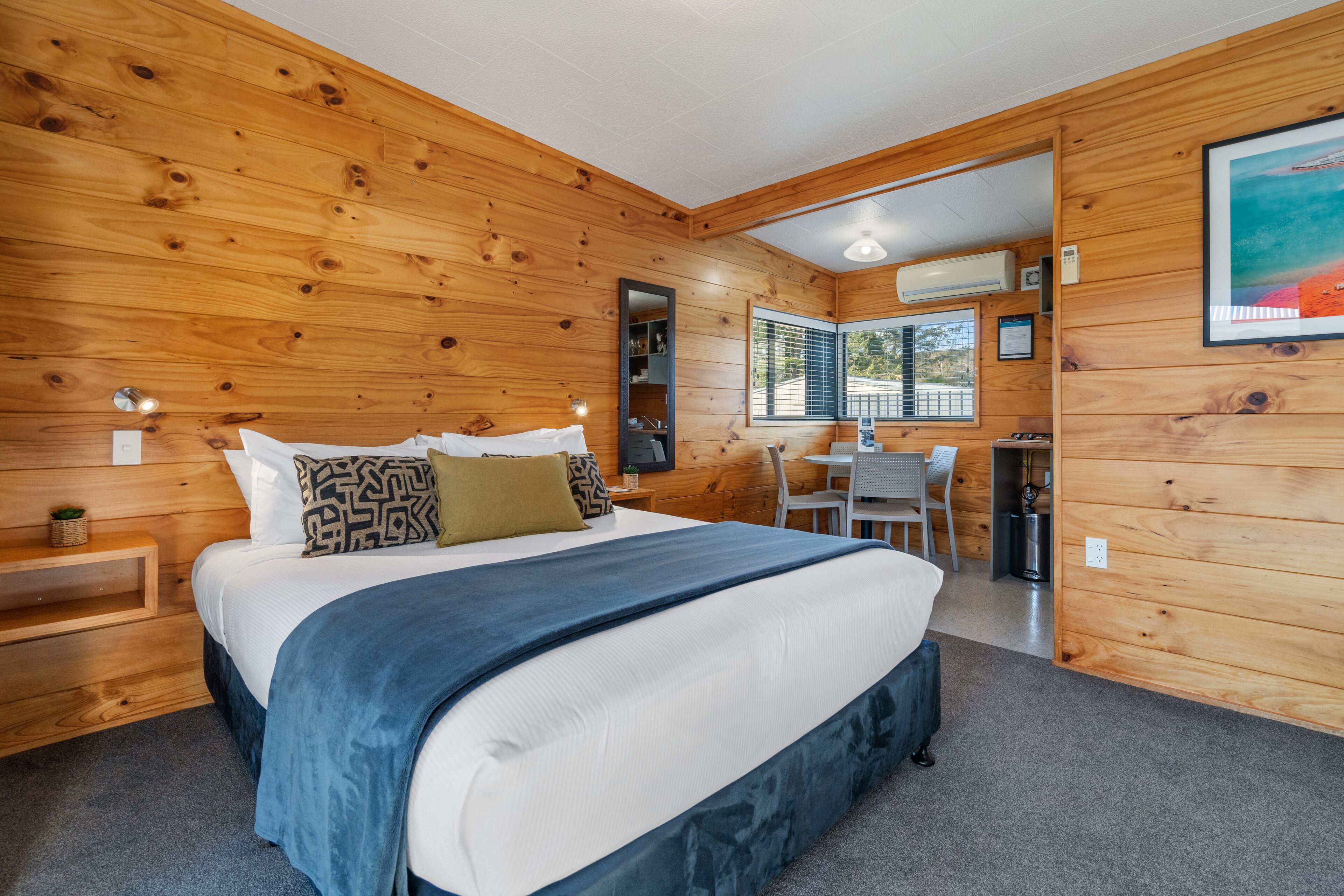 A wooden-paneled bedroom with a large bed, bedside tables, a desk, and a window.