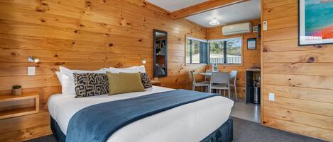 A wooden-paneled bedroom with a large bed, bedside tables, a desk, and a window.