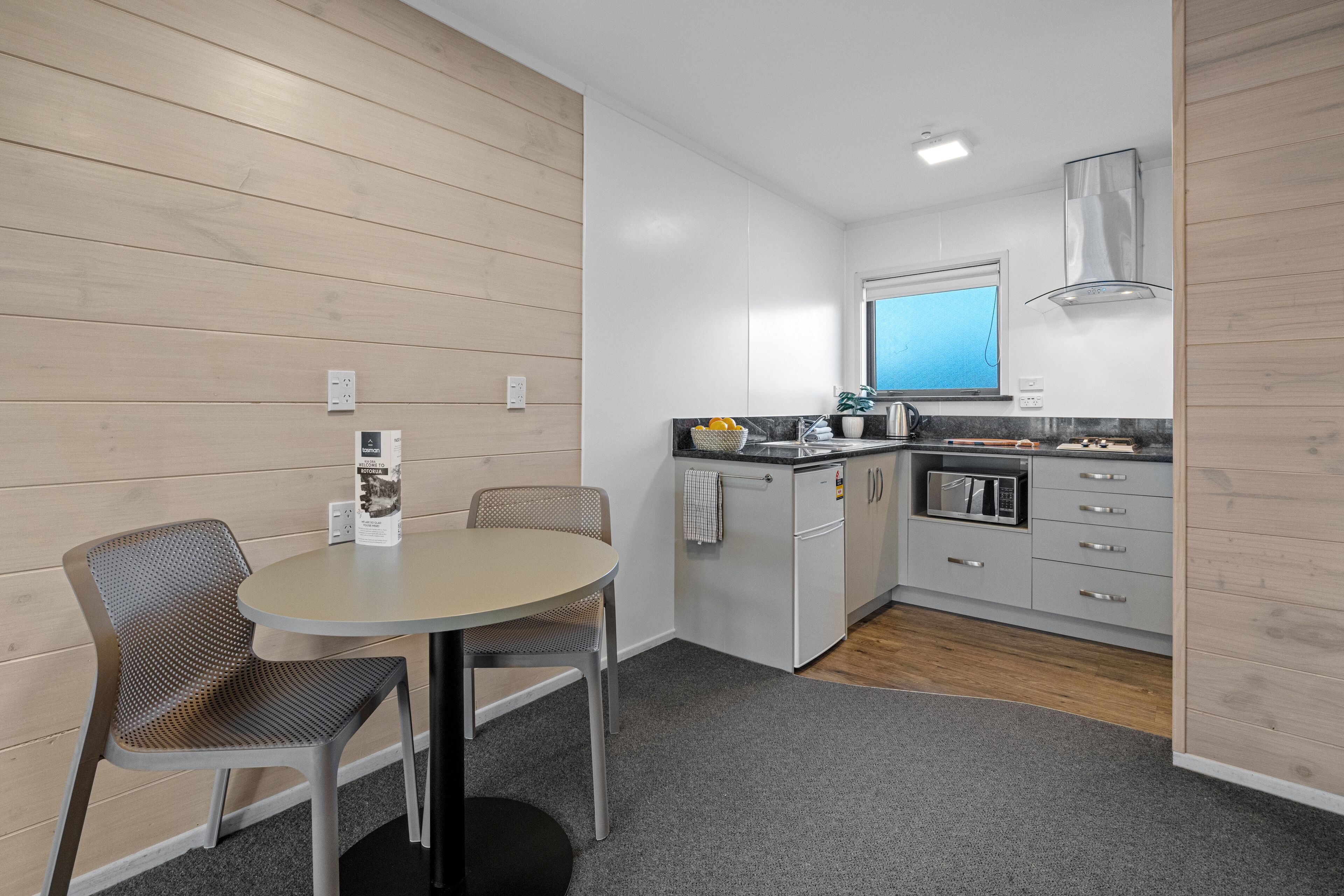 A compact kitchen with a dining area, featuring a round table, two chairs, a microwave, and a sink.