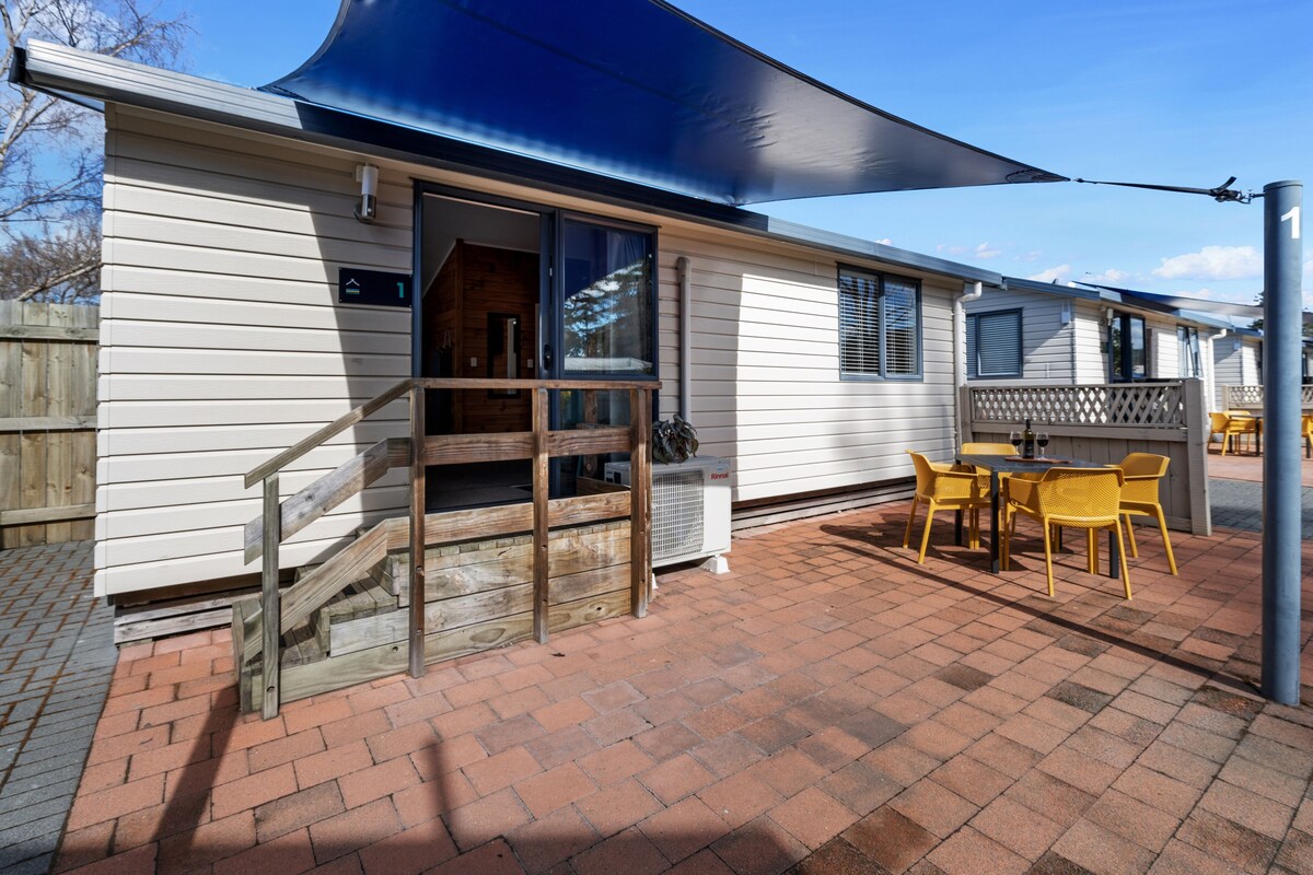 A mobile home with a patio area featuring a table and chairs, a staircase, and a large awning.