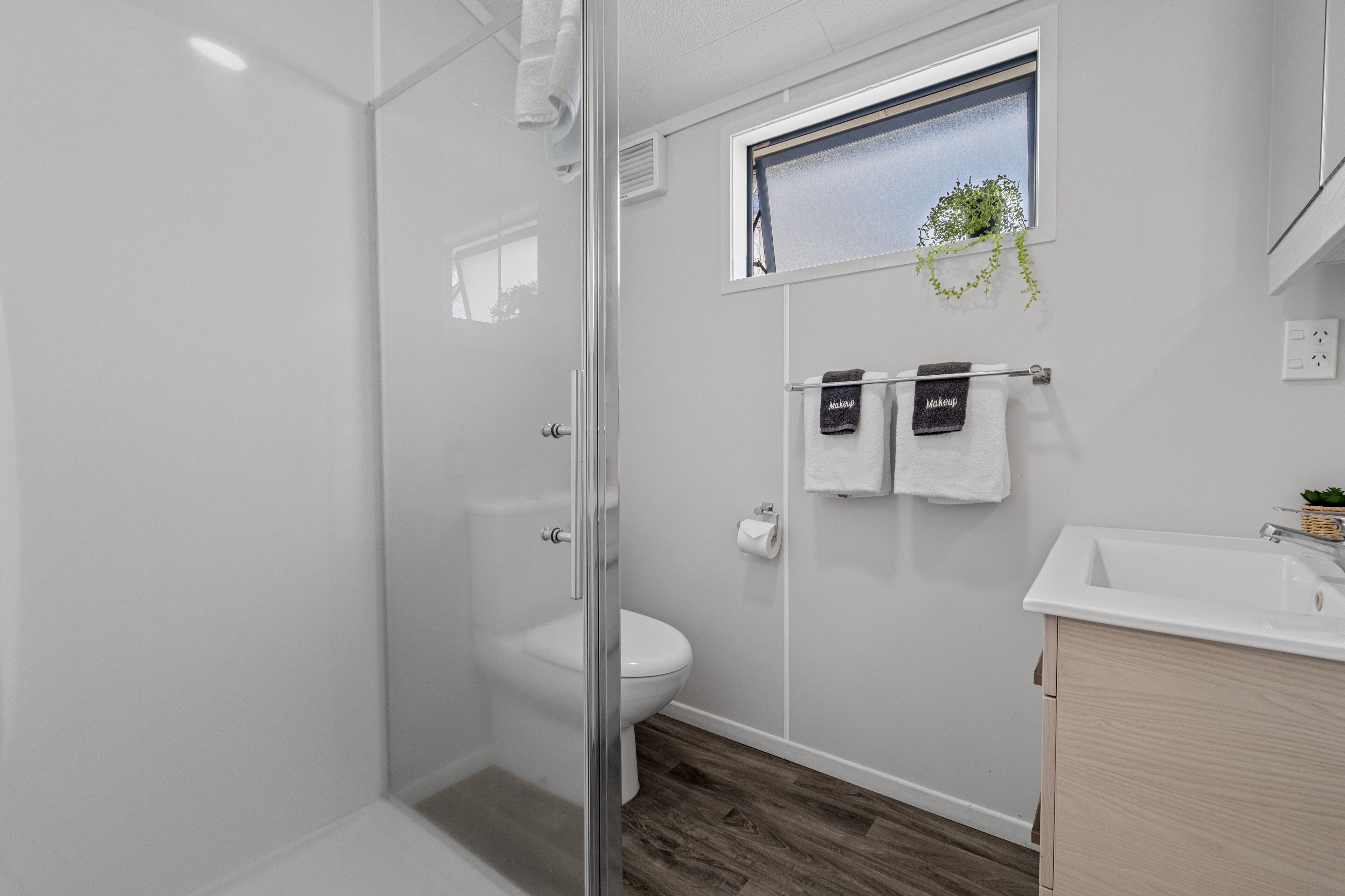 Een moderne badkamer met een douchecabine van glas, een toilet en een wastafel met houten opbergruimte.