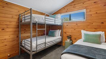 A bunk bed room with wooden walls, a single bed, and a window with blinds.