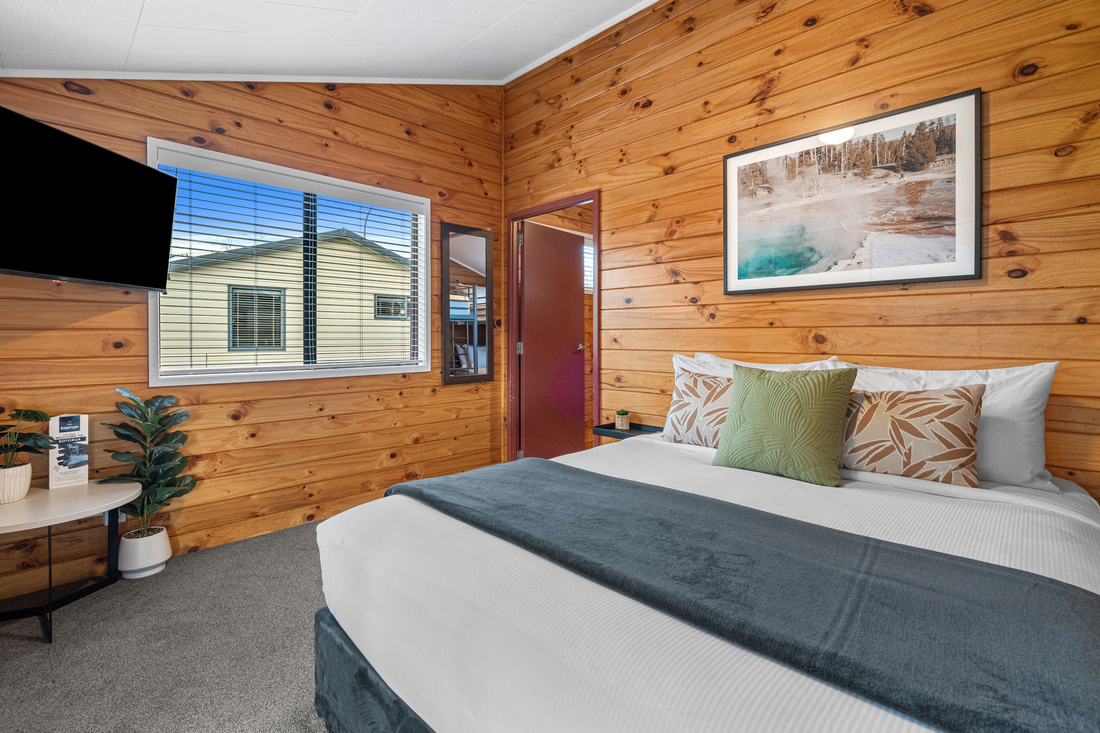 A wooden-paneled room with a bed, a TV, a window, and a door.