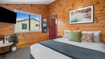 A wooden-paneled room with a bed, a TV, a window, and a door.