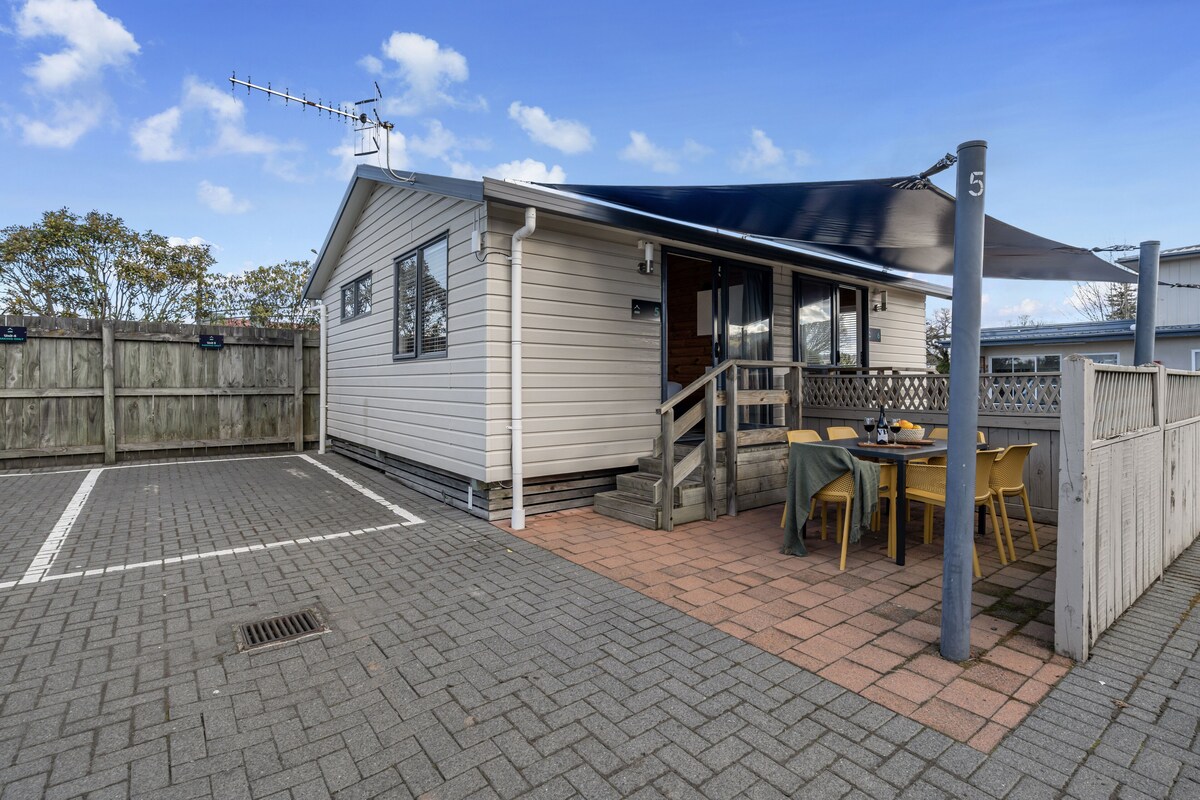 A small house with a patio area, a covered seating area, and a fenced yard.