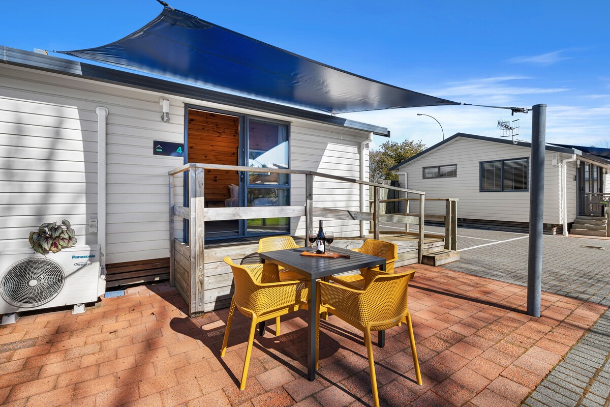 A mobile home with a patio area featuring a table and chairs, a fan, and a sign indicating the unit number.