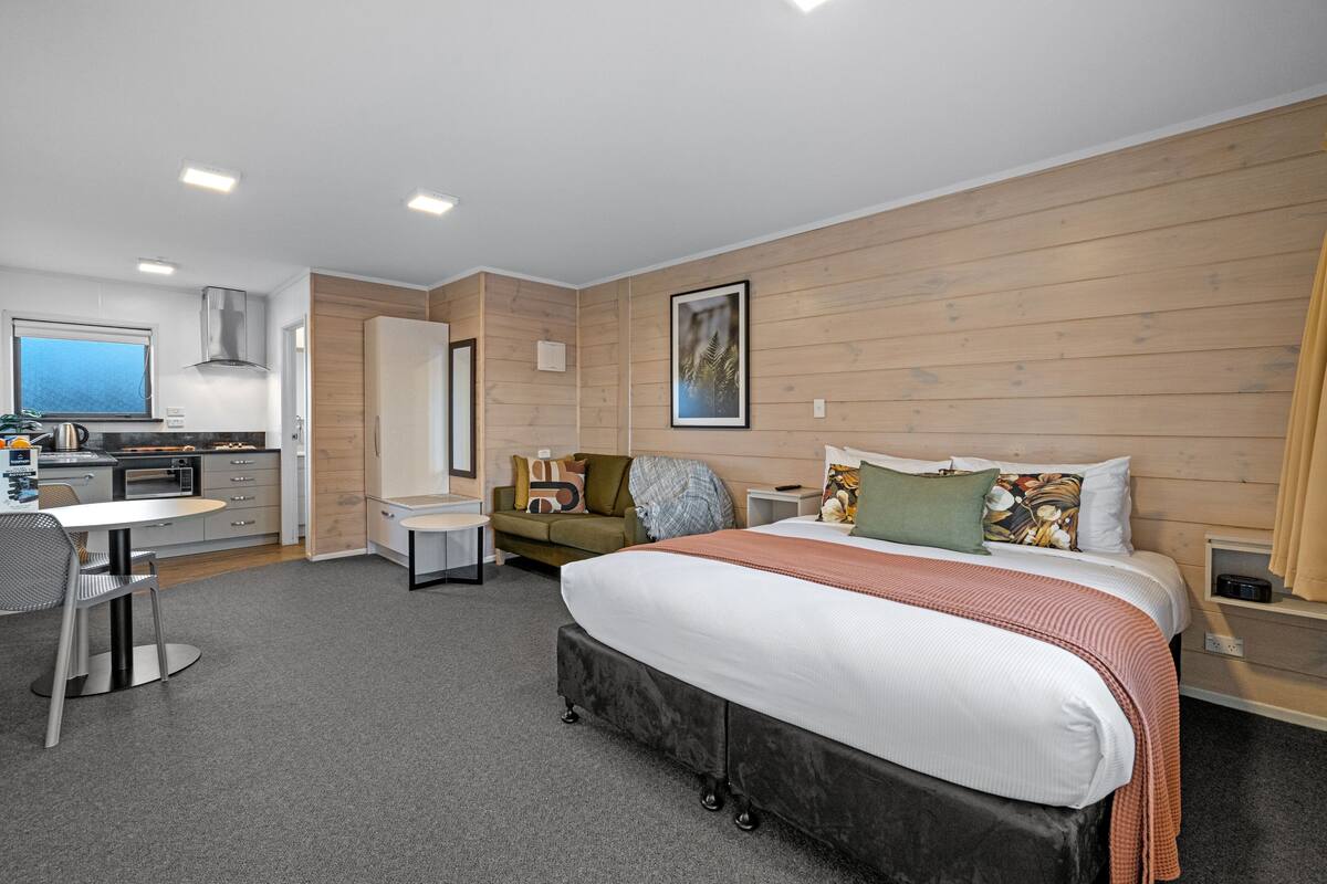 Una habitación de hotel moderna con una cama grande, un área de comedor, una kitchenette y vistas al mar.