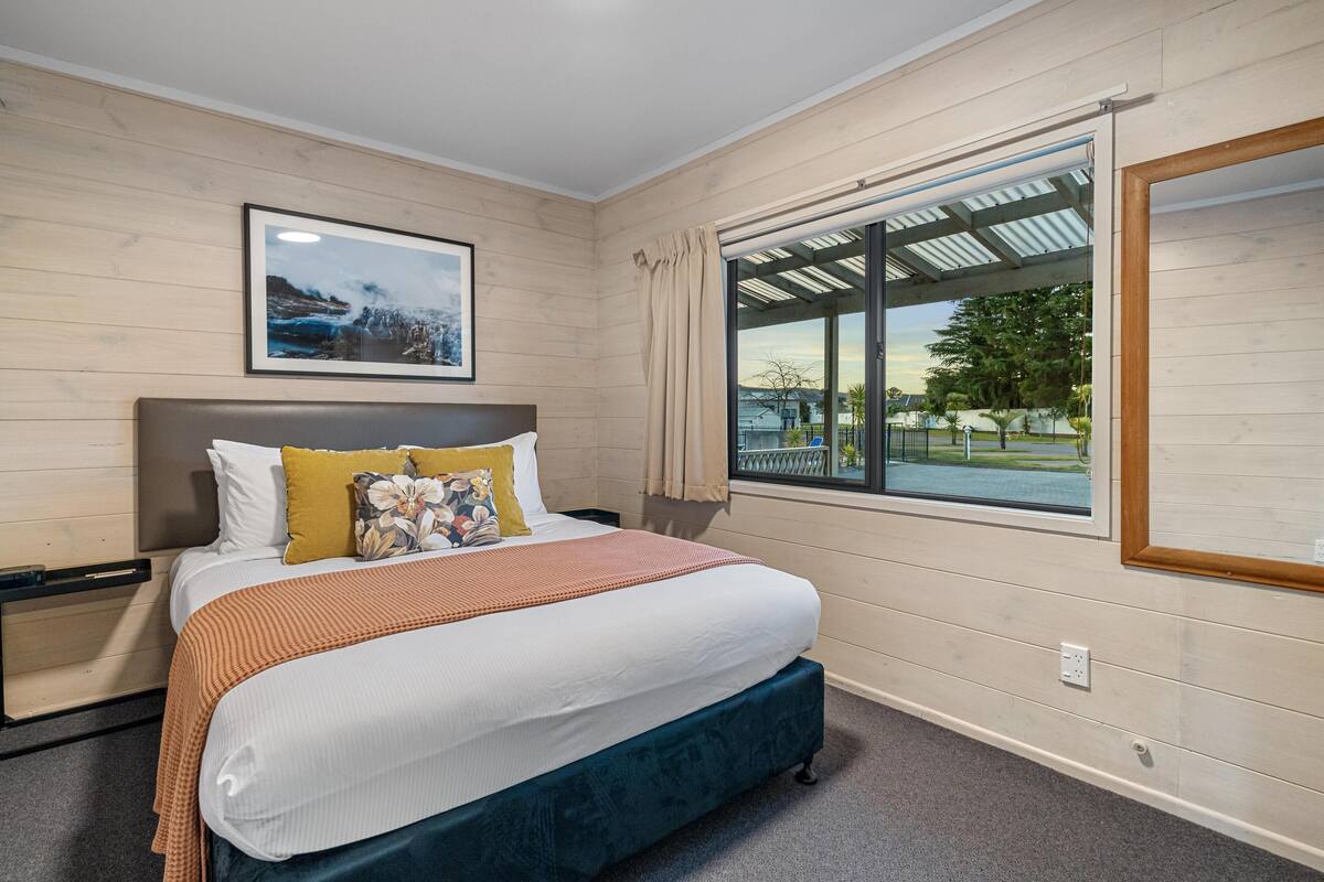 Un dormitorio con cama, ventana con vistas, cabecero y un cuadro en la pared.