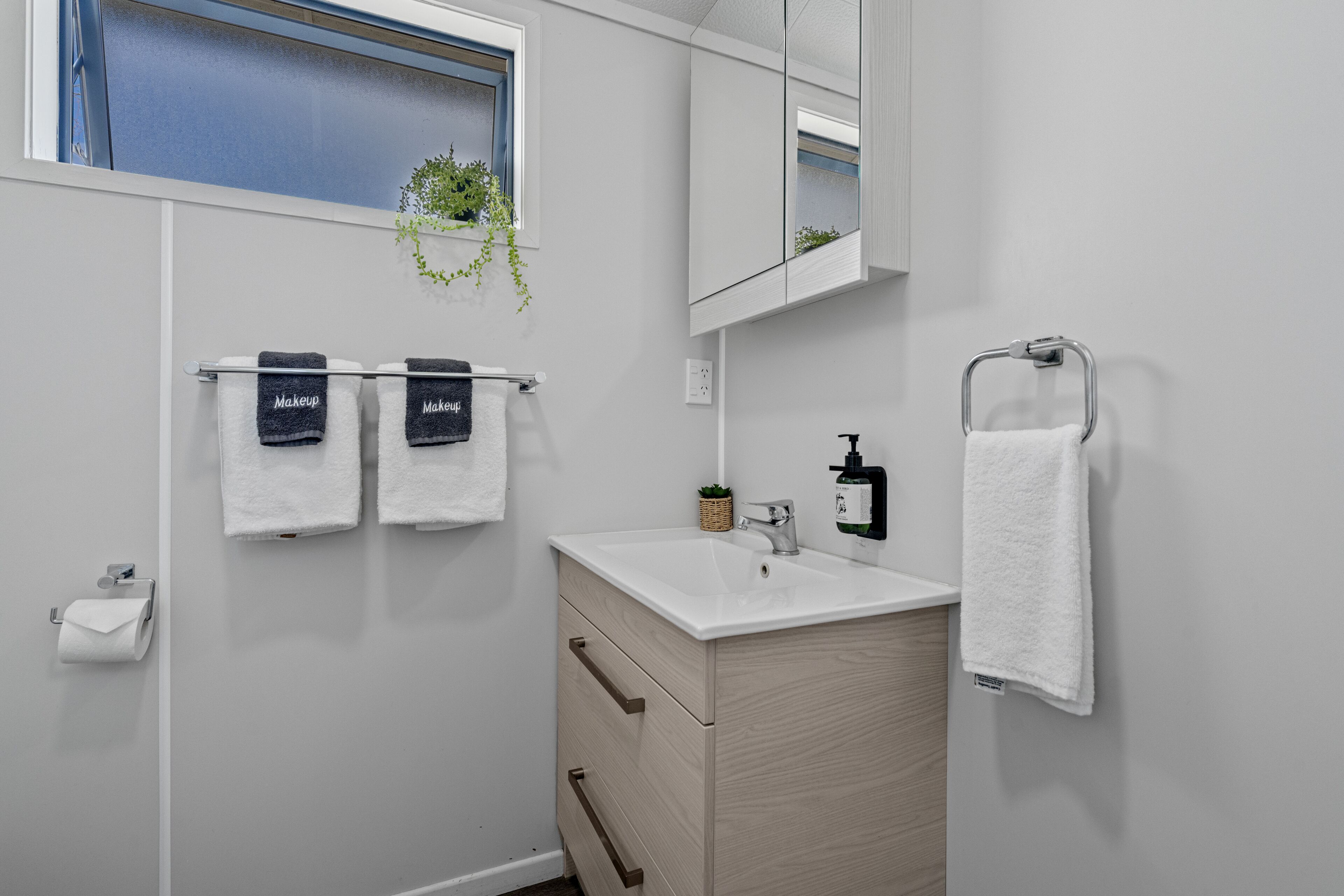Un baño moderno con un lavamanos blanco, un espejo y dos toallas colgadas en un perchero.