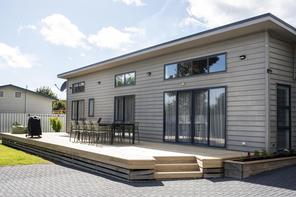 A modern two-story house with a patio, outdoor seating, and a large sliding glass door.