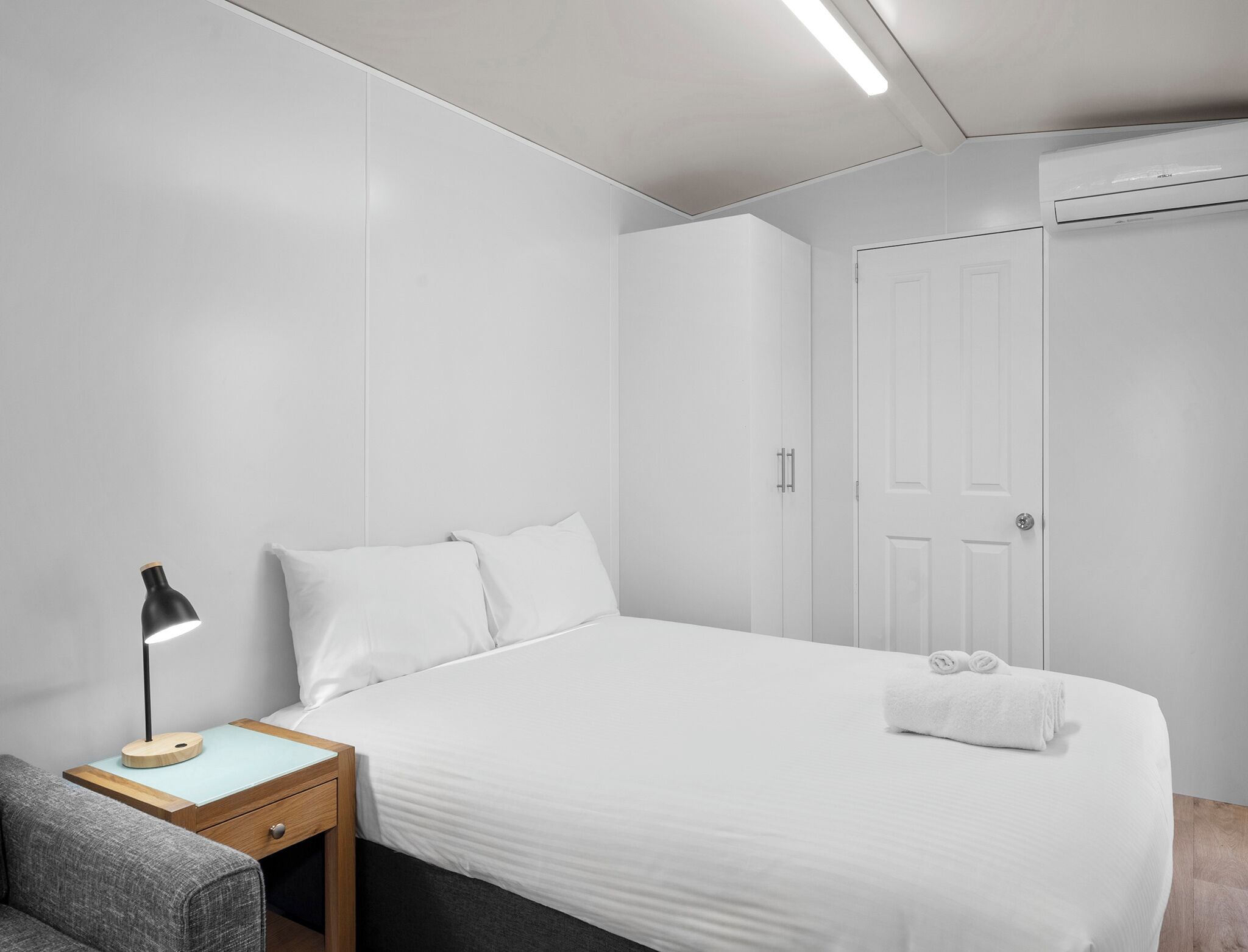 Una habitación de hotel moderna con una cama bien hecha, una mesita de noche con lámpara y un armario.