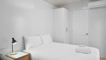 Una habitación de hotel moderna con una cama bien hecha, una mesita de noche con lámpara y un armario.