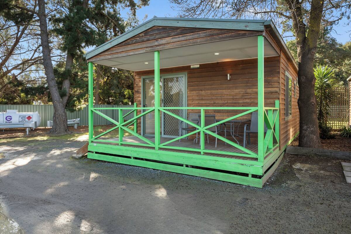 A small wooden cabin with a green porch and a covered patio area.