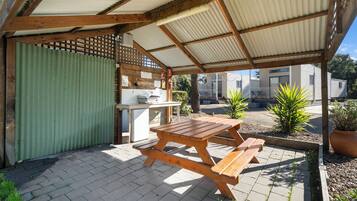 A covered outdoor area with a wooden picnic table, a grill, and a green gate.