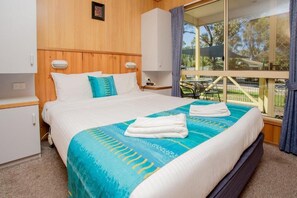 Ein Schlafzimmer mit einem Bett, einem Holzkopfende, weißen Nachttischen und einem Fenster mit Blick auf einen Park.