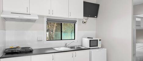 A compact kitchen with white cabinets, a black countertop, a built-in microwave, and a window with a view of trees.