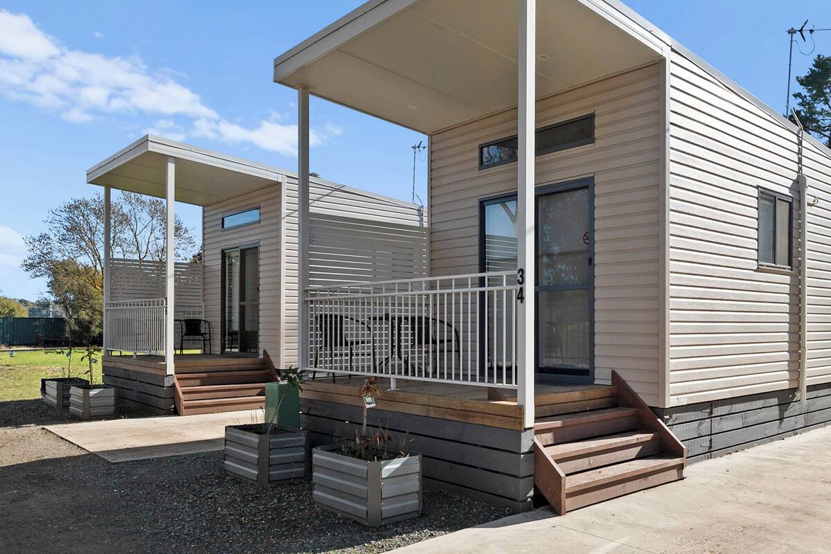 A modern, two-story mobile home with a covered porch and a small deck area.