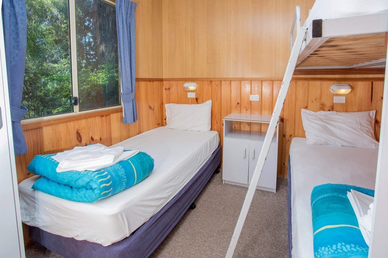 A cabin with two beds, a small white cabinet, and a window with curtains.