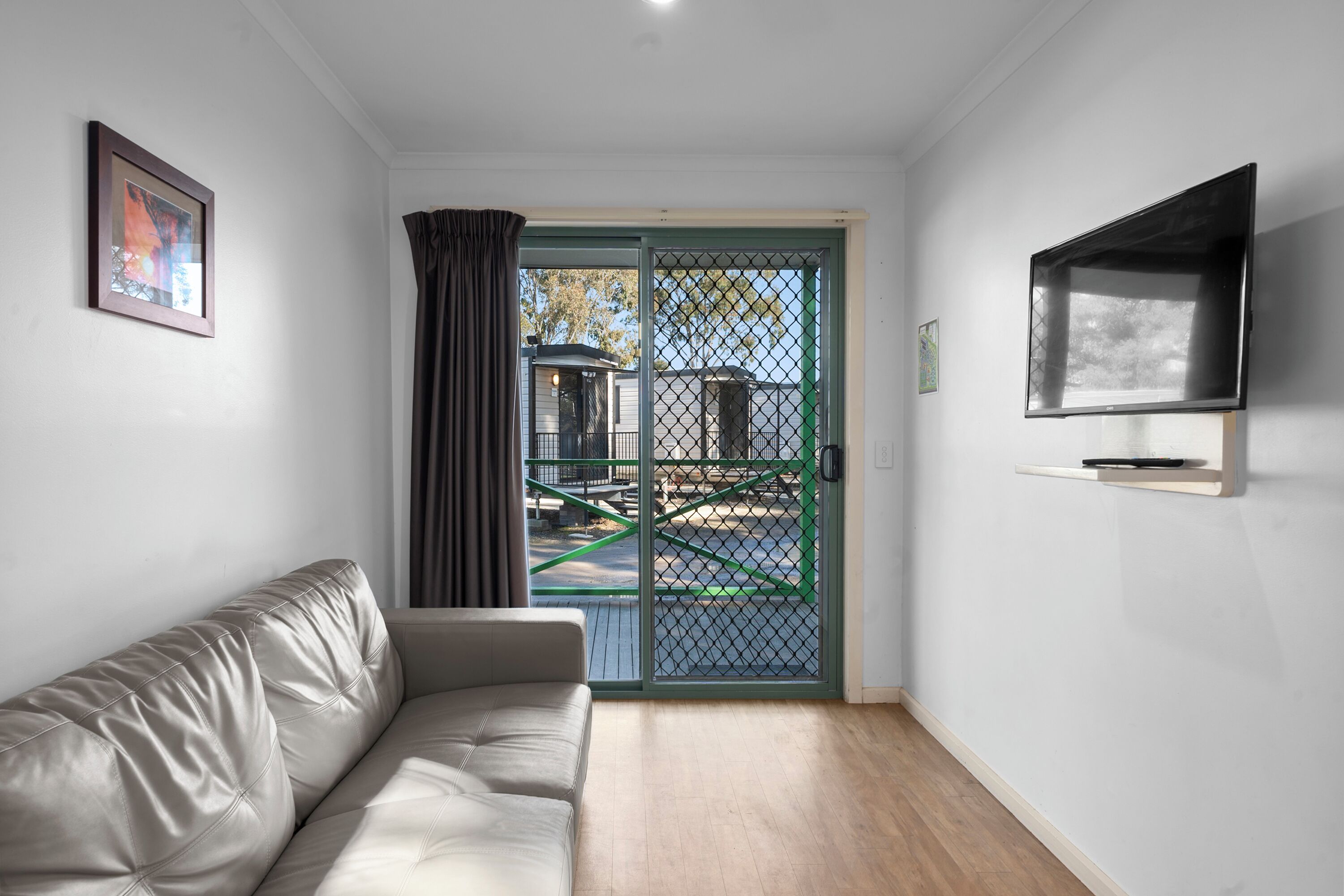 A modern living room with a leather sofa, a TV mounted on the wall, and a sliding glass door leading to an outdoor area.