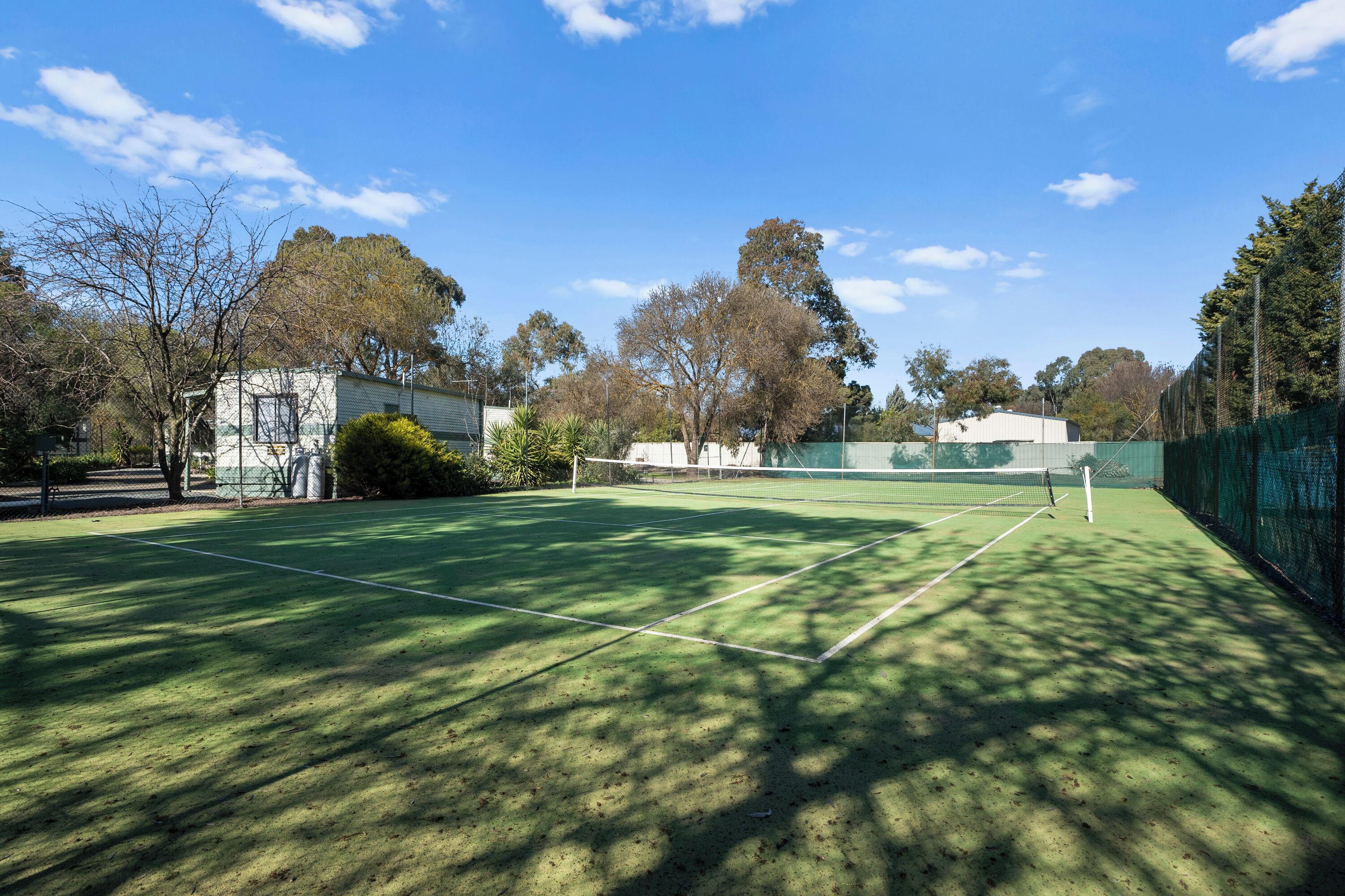 A tennis court with a net, surrounded by trees and buildings.
