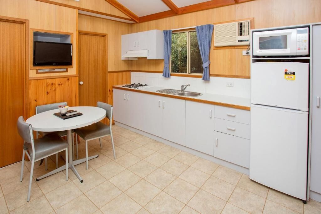 A compact kitchen with white cabinets, a gas stove, a sink, a microwave, and a small dining table with chairs.