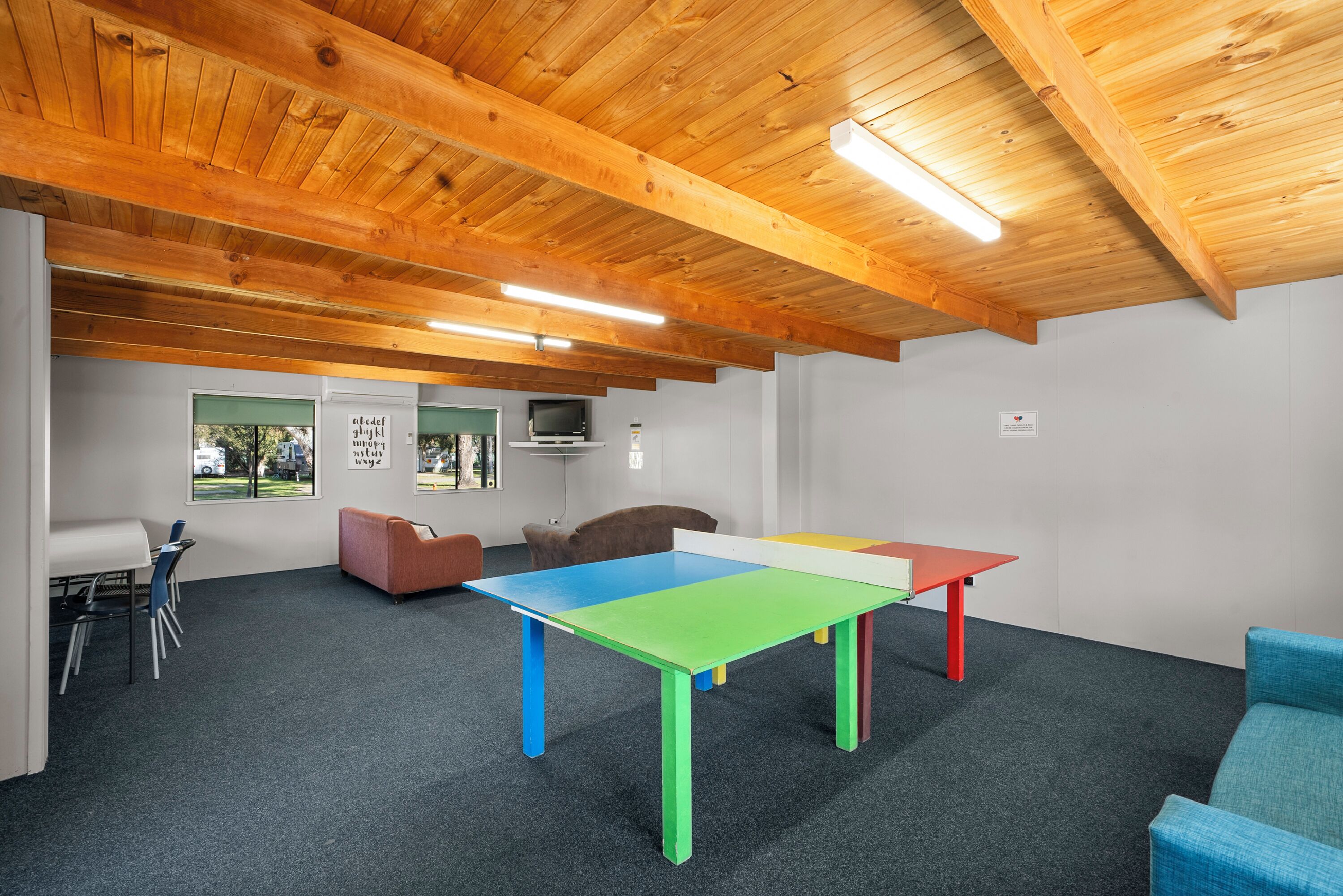 A room with a wooden ceiling, a colorful table, a sofa, and a TV.