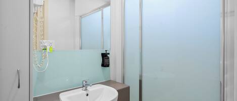 A bathroom with a white sink, a mirror, and a glass shower enclosure.