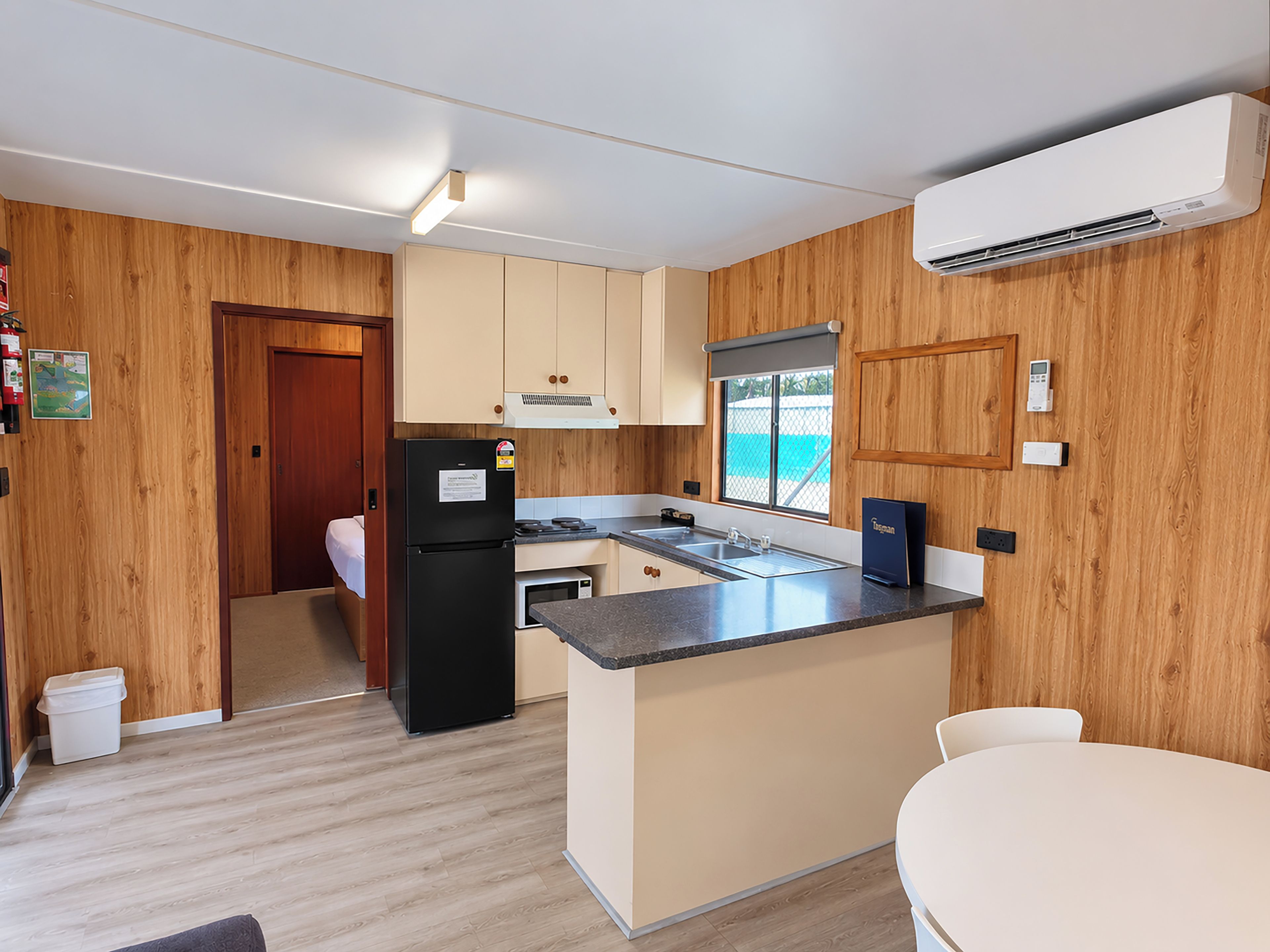 A compact kitchen with wooden paneling, a built-in refrigerator, a microwave, and a window with a view.