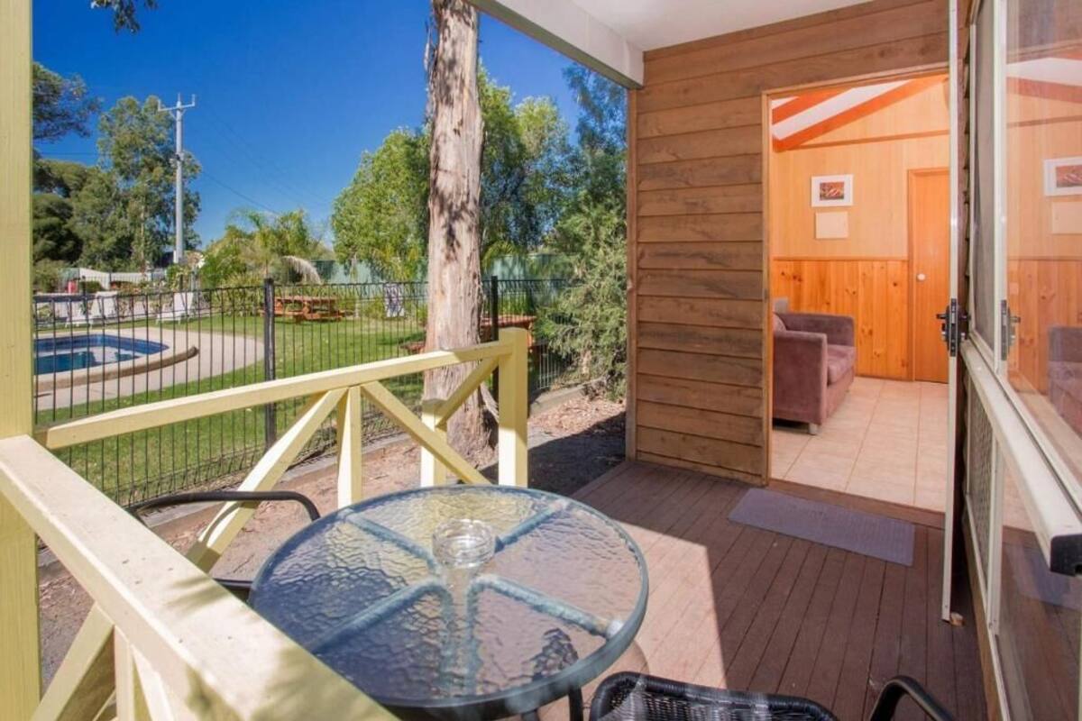 A glass-top table on a wooden deck with a view of a fenced area and trees.