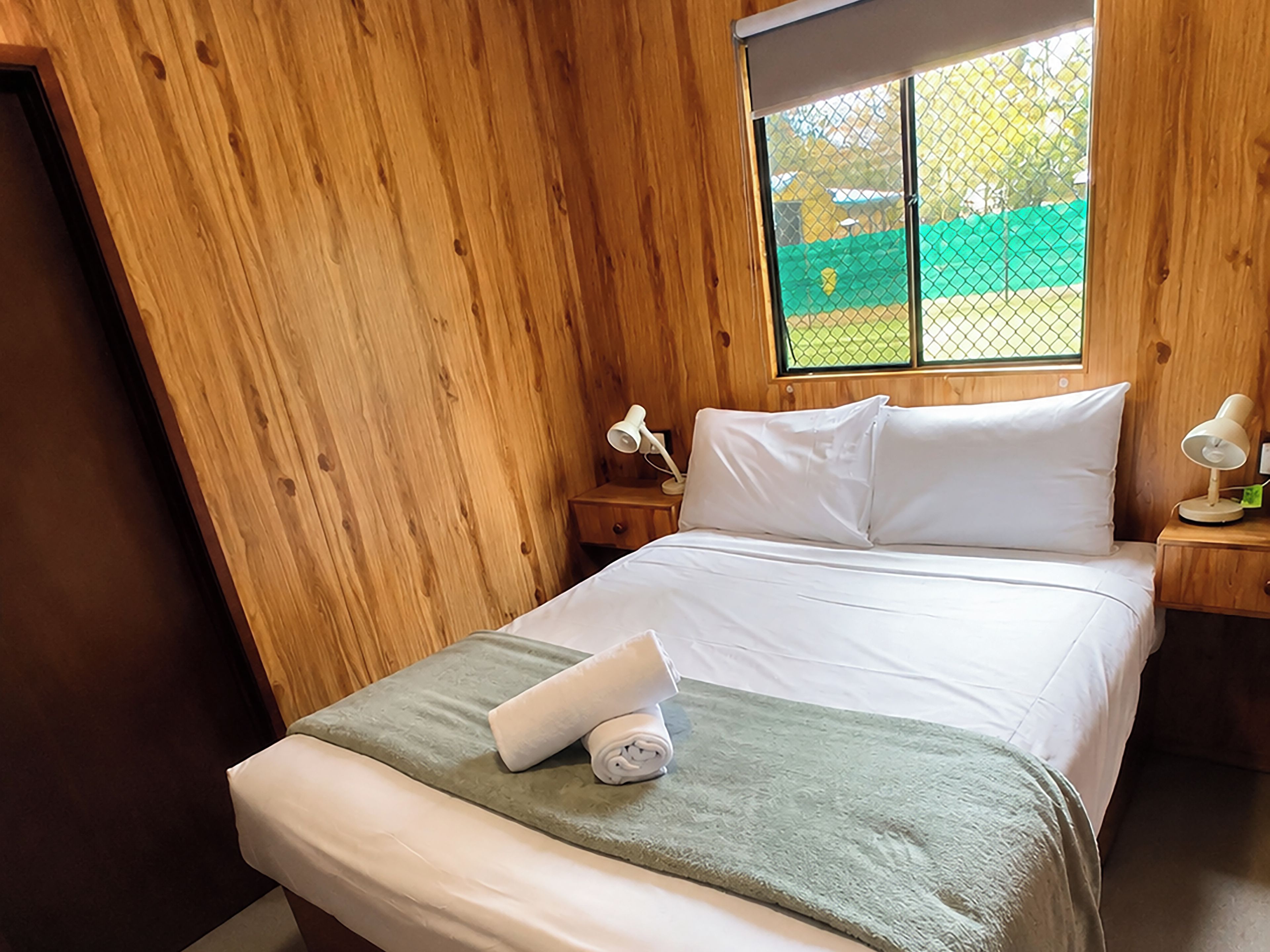 Une pièce en bois avec un lit, une fenêtre et une table de chevet avec une lampe.