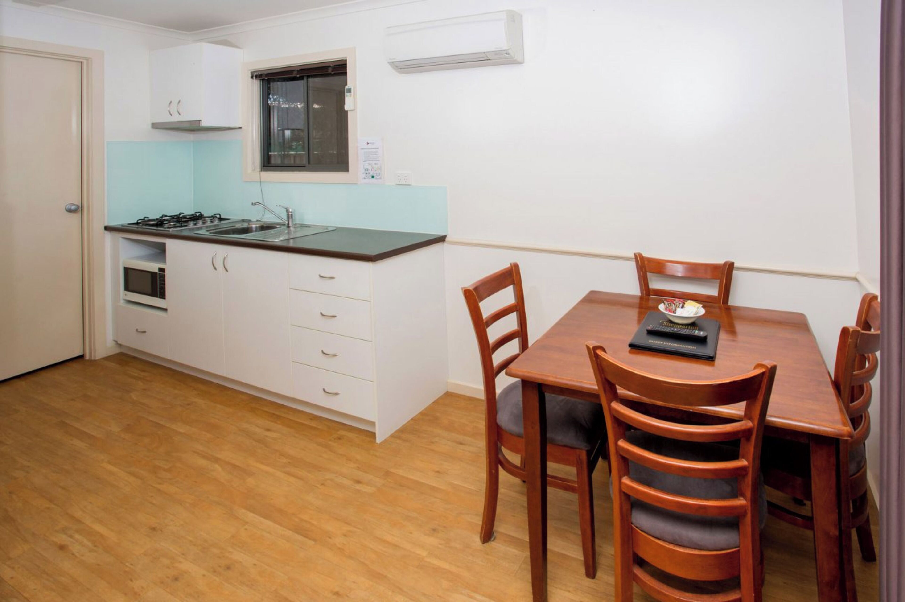 A compact kitchen with a stove, sink, and white cabinets. There is a dining table with four chairs and a window above it.