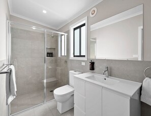 Ein modernes Badezimmer mit einer Duschkabine aus Glas, Toilette, Waschbecken und einem großen Spiegel.