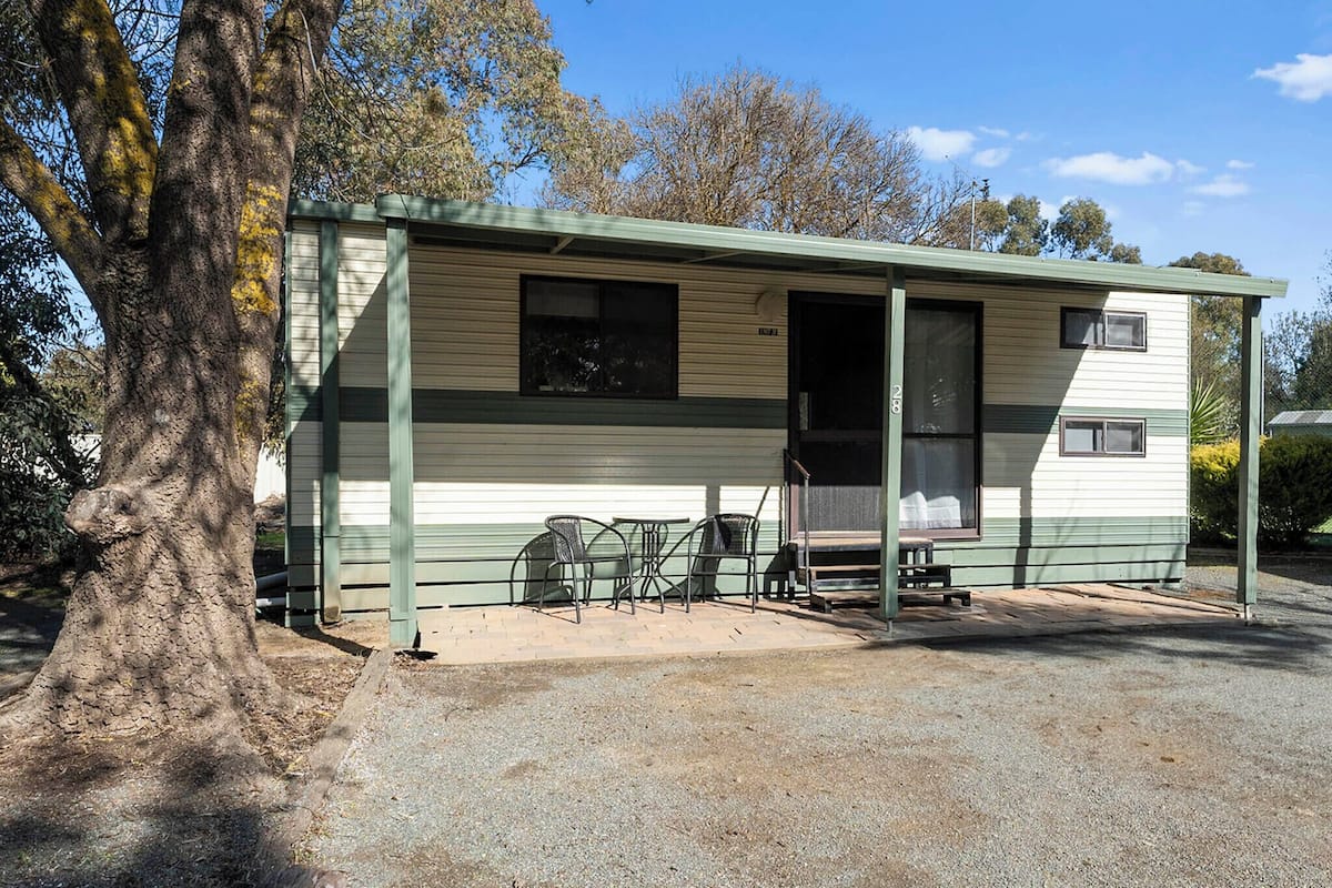 A single-story mobile home with a porch, a small table, and chairs.