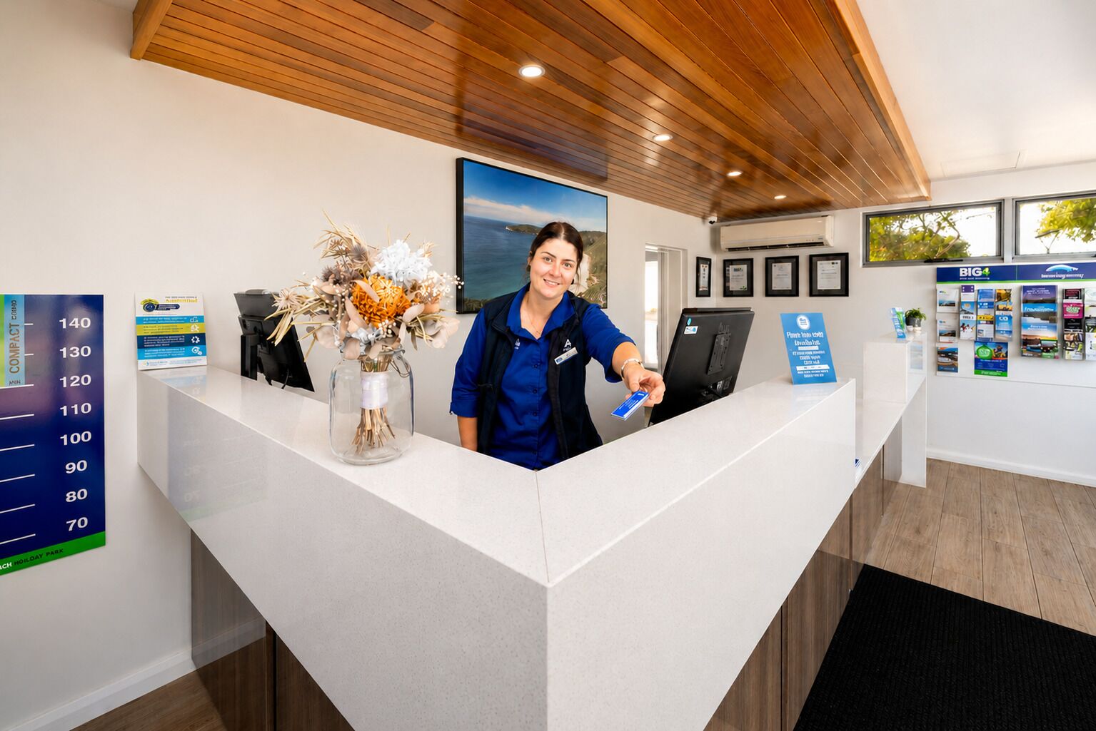 A reception desk with a large floral arrangement, a digital display, and informational posters on the wall.