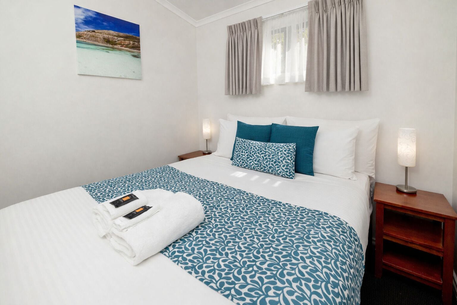 A hotel room with a bed, a nightstand, a lamp, and a painting on the wall.