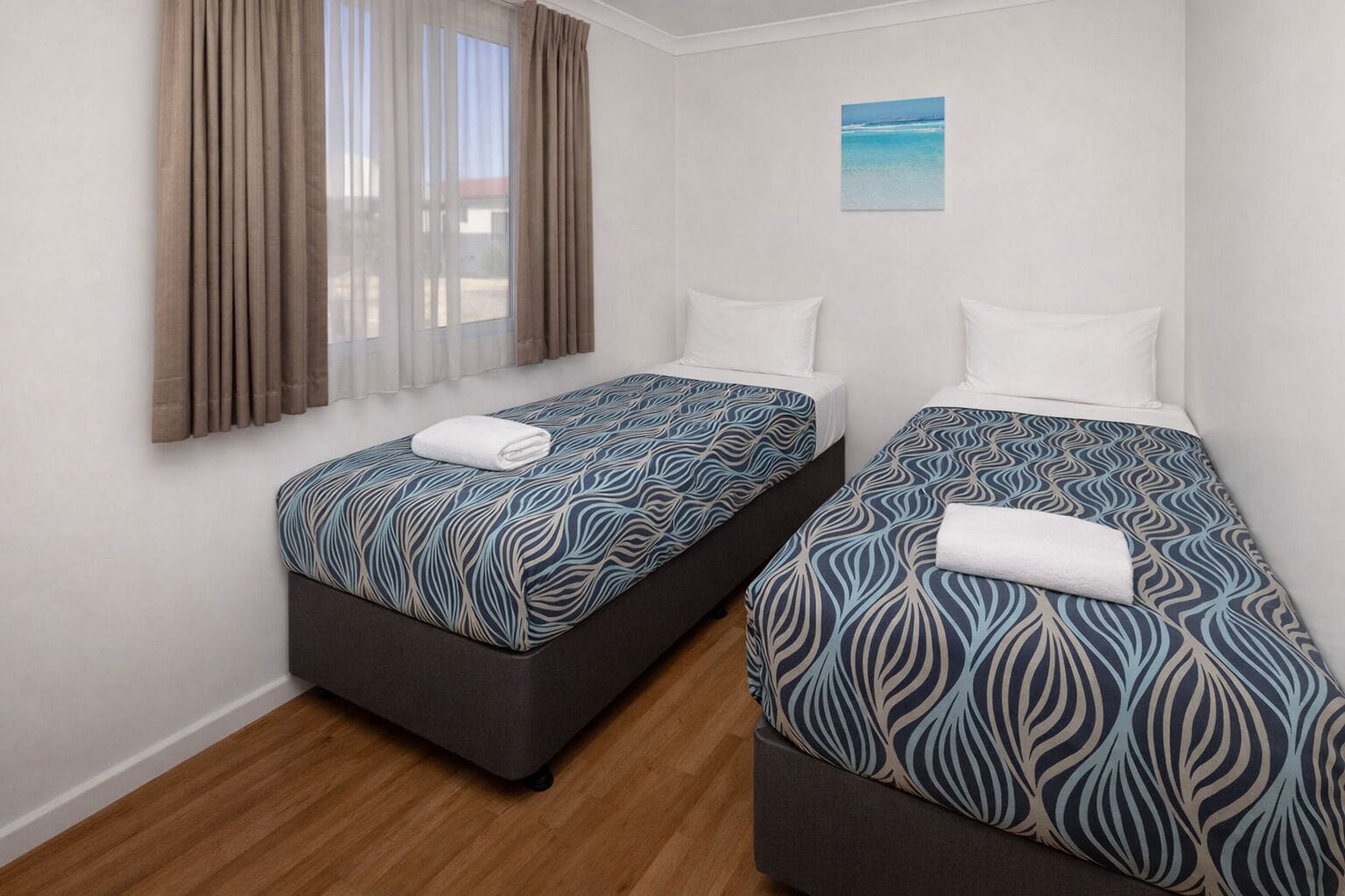 Una habitación de hotel con dos camas, una ventana con cortinas y un pequeño cuadro en la pared.