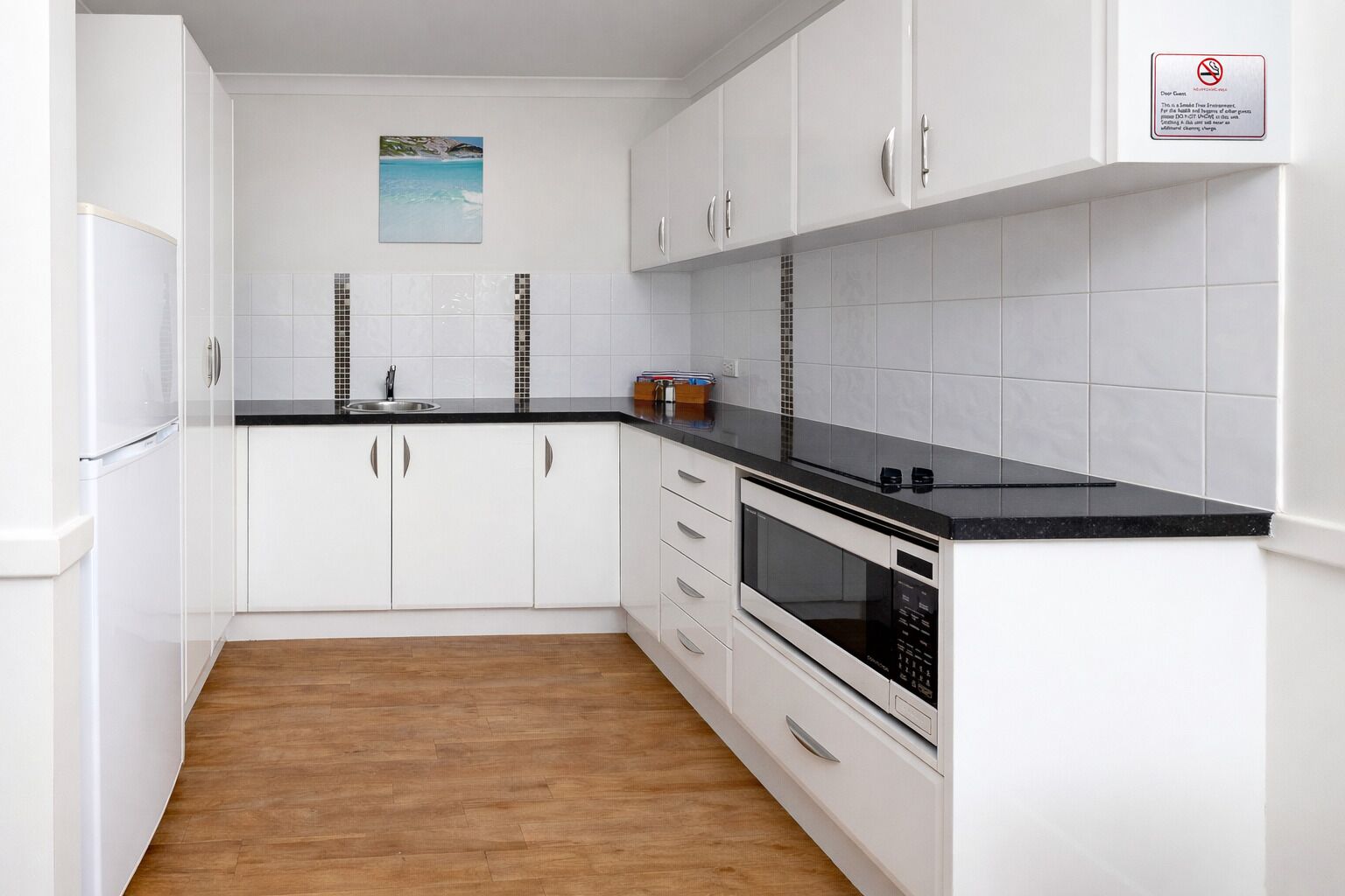 Una cocina moderna con armarios blancos, encimera negra y suelo de madera.